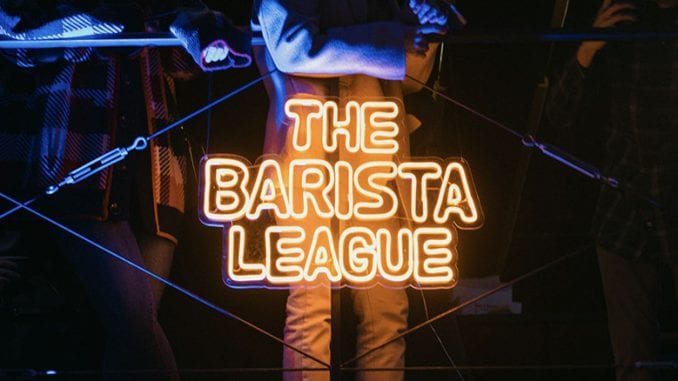 A night time image of the bottom half of a person. The Barista League is in a yellow neon sign.