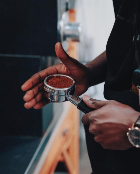 A closeup of Baidy's hands leveling out coffee grounds in an espresso tamper.