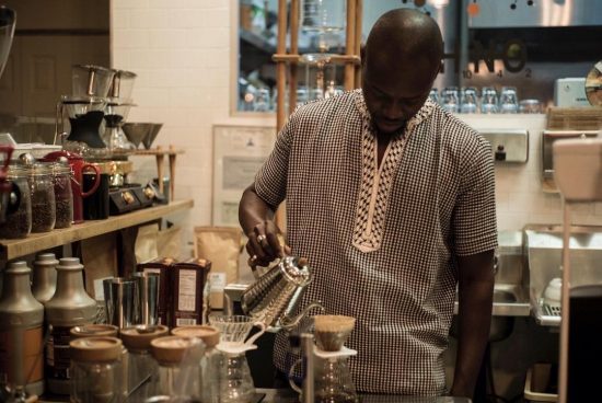 Baidy at a distance pouring water over a bed of coffee grounds. Here is using a pourover.