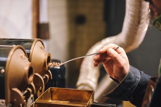 Pauls hand holding a spoon full of coffee. He puts this into a metal sample roaster.