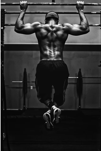 A black and white photo, featuring a man doing pull ups. Only his backside is exposed.