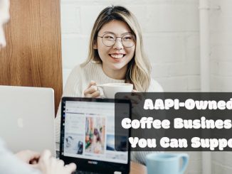 The title cover says AAPI businesses you can support. In the middle is an Asian female smiling. She has dyed blonde hair and wears glasses. She holds a coffee cup smiling and looking off the camera. There is a laptop in front of her and she is at a coffee shop.