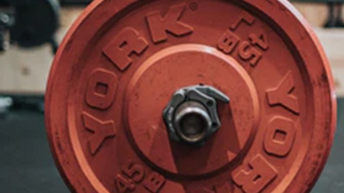 A single red plate of a weight sits on a gym mat.