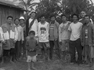 A black and white photo. Several people crowd together with their arms around each other on an island in the Philippines.