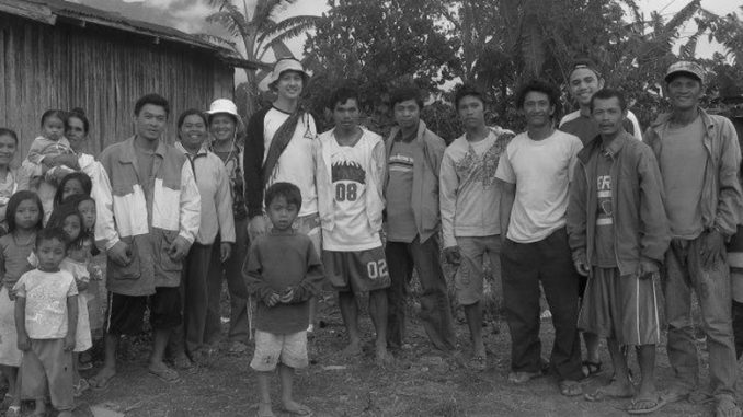 A black and white photo. Several people crowd together with their arms around each other on an island in the Philippines.