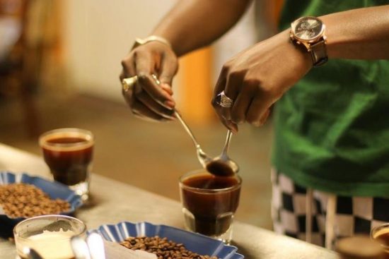 A closeup of Baidy's hands scooping coffee grounds of up a cupping bowl.