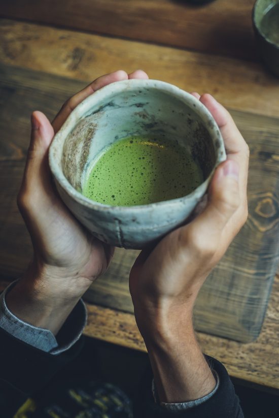 A closeup shot of hands holding a ceramic mug with matcha water.