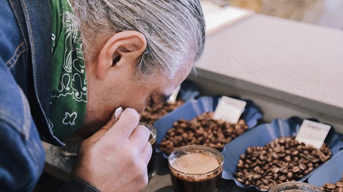 Paul is a man in his mid 40s, we see a side profile of him with his face close to brewed coffee samples. He is cupping them.