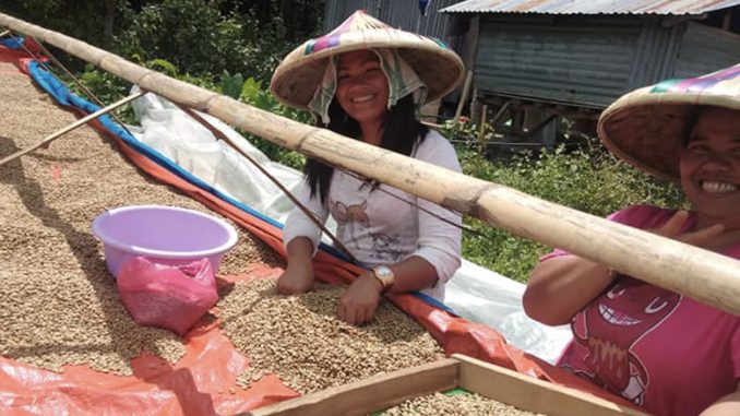 Two Filipino coffee producers stand in front of drying coffee while smiling.