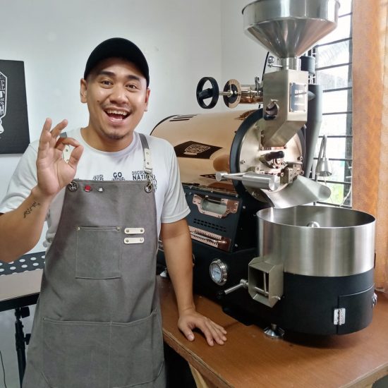 A man in front of a coffee roaster smiling.
