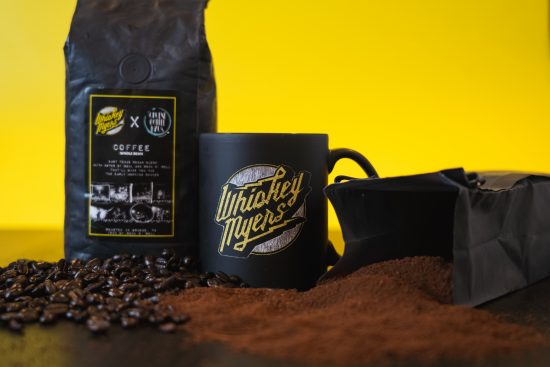 A closeup of the bag and mug. They are both black with black labeling. The mug has Whisky Myers in lightning font across it.