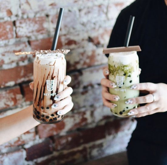 Two hands hold cocktail glasses filled with milky beverages. At the bottom are boba pearls.