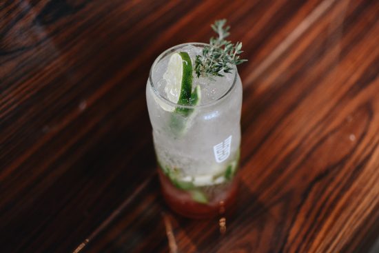 A closeup of a cocktail glass filled with a light green beverage. It is topped with a mint leaf and a cucumber slice.