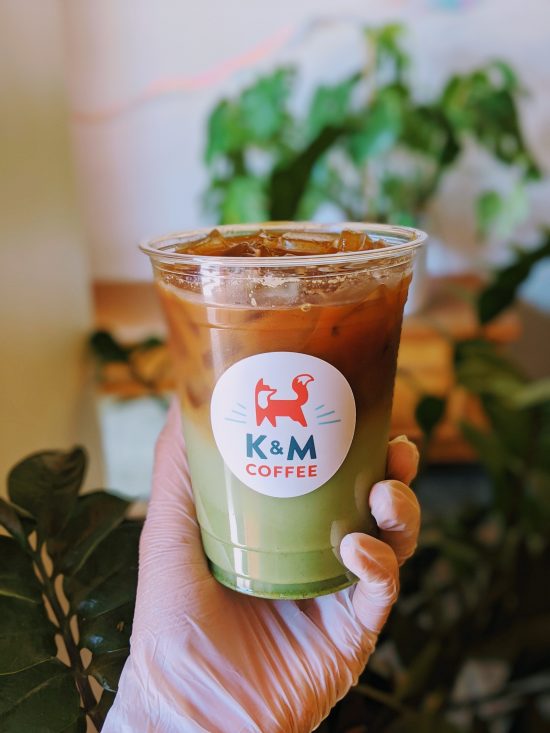 A coffee shop holds up their pandan drink. It is in a plastic cup with brown on the top and green on the bottom.