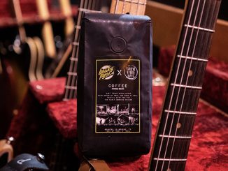 A closeup of a black coffee bag of beans. It stands amidst a set of electric guitars.