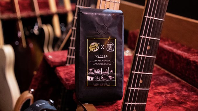 A closeup of a black coffee bag of beans. It stands amidst a set of electric guitars.