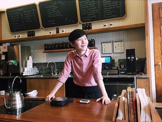 Peace wears a pink collared shirt and smiles looking to the right. She is at the counter of the Stumptown brew bar.