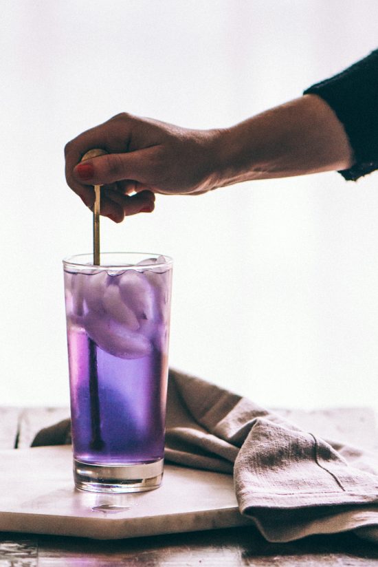 An iced purple drink with a hand stirring it.