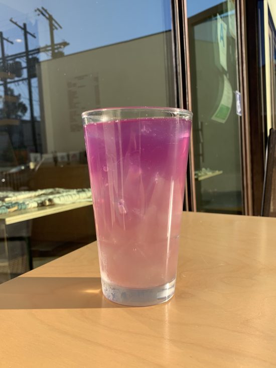 An iced drink on a table in the sunlight. It is a mix of pink and lemonade.