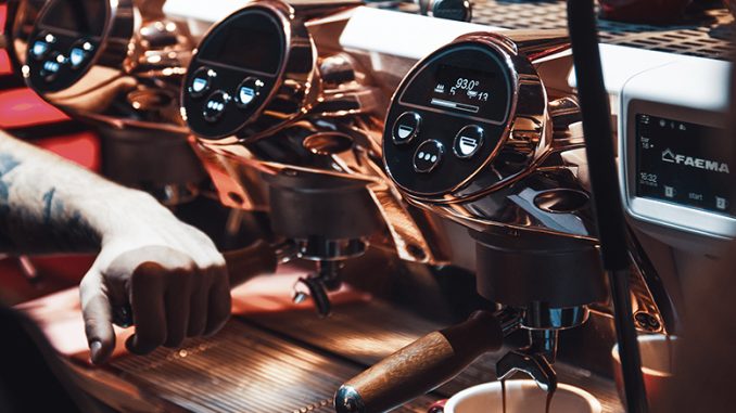 A closeup of a barista using a Faema espresso machine.