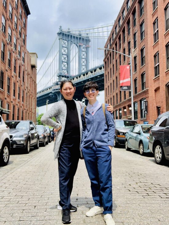 Peace and her mom stand in front of a bridge in New York City. They both smile.
