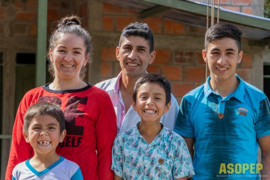 A family from the ASOPEP cooperative stands smiling. There is a mother, father, and three sons.