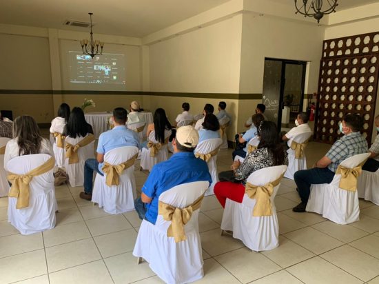 A group of people sit with their backs facing the camera. They are watching the awards ceremony on a screen.