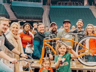 A group of people stand in a stadium smiling holding bikes.