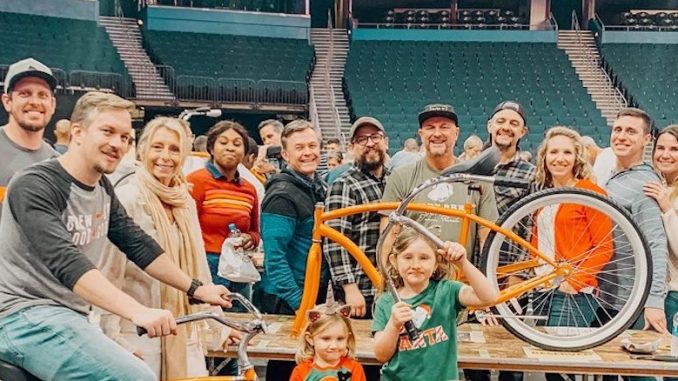 A group of people stand in a stadium smiling holding bikes.