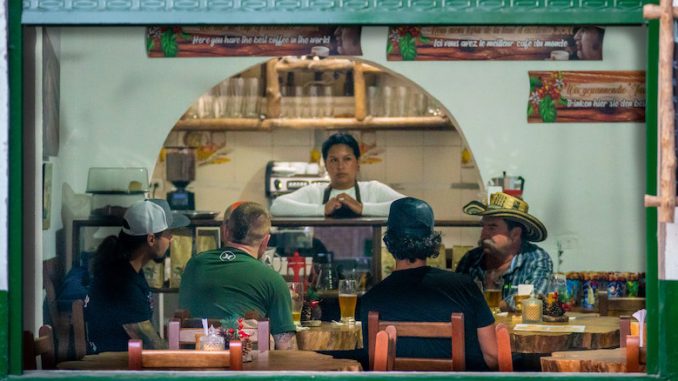 The interior of a food business shows the back of several patrons eating at a takeout window.