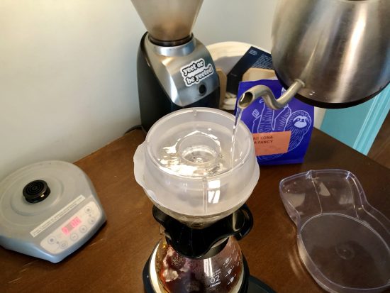 A gooseneck kettle pours water into a v60 with the drip assist sitting on top.