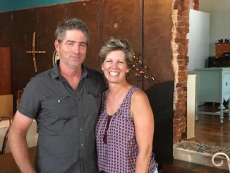 Kasey Towles and her husband Randy. Both are smiling, have short hair. Kasey is blonde and wears a red tank top, Randy a brown collared shirt. They are inside their business.
