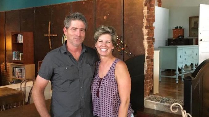 Kasey Towles and her husband Randy. Both are smiling, have short hair. Kasey is blonde and wears a red tank top, Randy a brown collared shirt. They are inside their business.