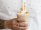 A closeup of a torso in a white polka dot colored shirt. They are holding a frappuccino.