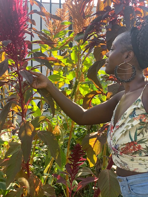 The owner Kymme volunteering at an urban farm in Brooklyn. She looks to the left holding a leaf.