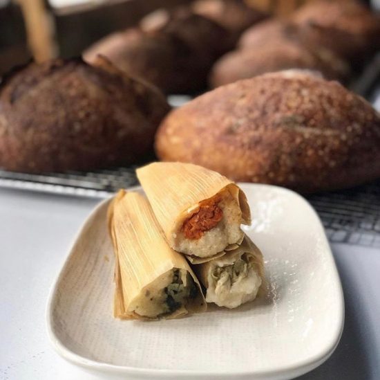 A closeup of three tamales sitting on a white plate on a counter.