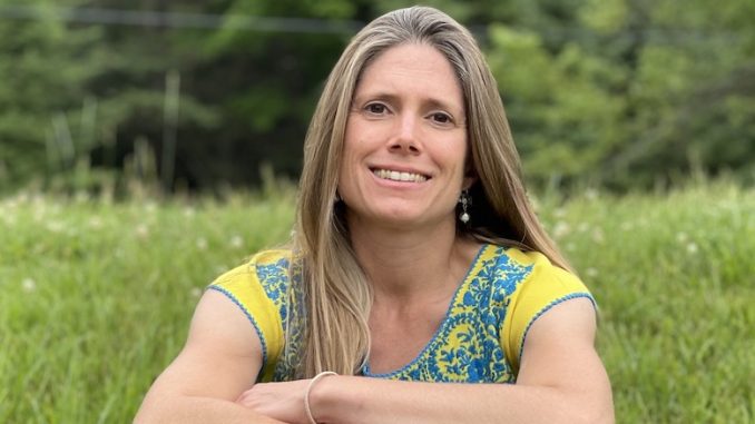 Alyson Welch in a blonde white woman in her 40s. She poses with her arms crossed smiling in a grassy field.