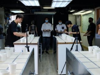 A group of people gather to taste coffees out of paper cups in a classroom lighting indoors space.