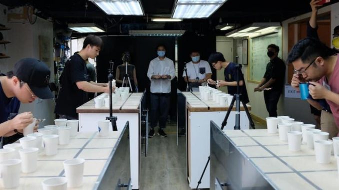 A group of people gather to taste coffees out of paper cups in a classroom lighting indoors space.