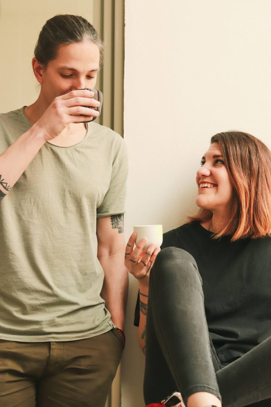 Alan is about 6'2. He stands drinking a coffee next to his partner, a woman with medium length dyed orange hair who looks up at him smiling.