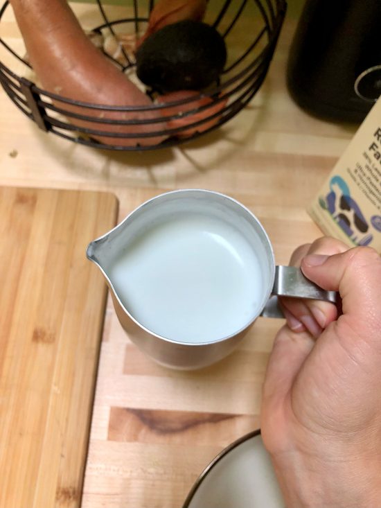 A closeup of hands holding a pitcher with milk in it.