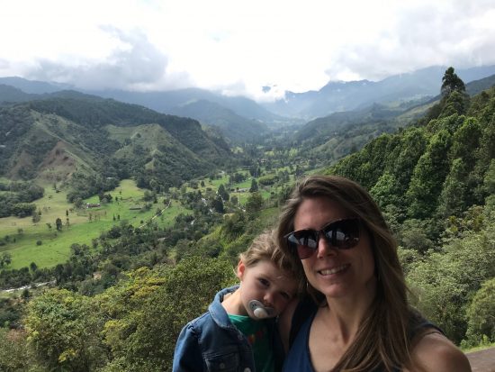 Aly stands with her toddler son in a valley that grows coffee.