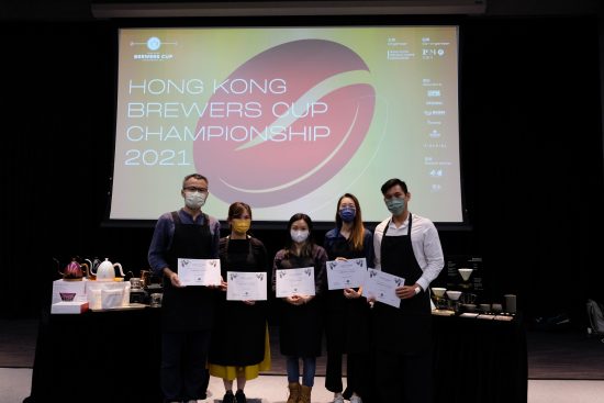 The judges and winners stand in a line together posing for photos in front of a projector with the results.