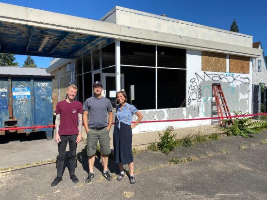 Three people stand in front of a torn down gas station. It has not started with construction yet.