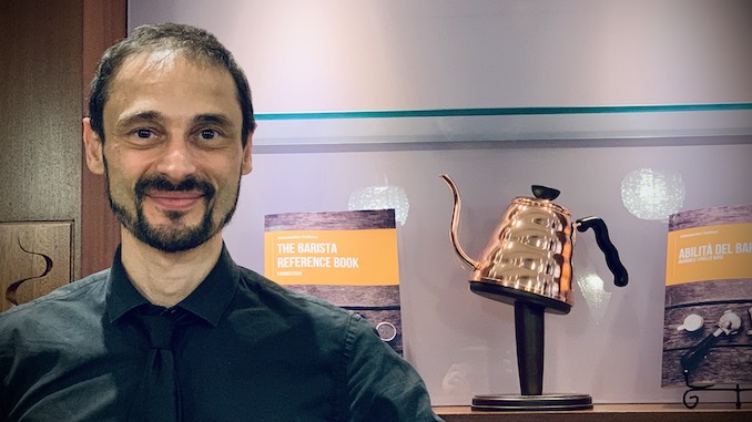 Alessandro is an Italian man in his 40s. He smiles with his teeth closed next to his championship kettle and book.