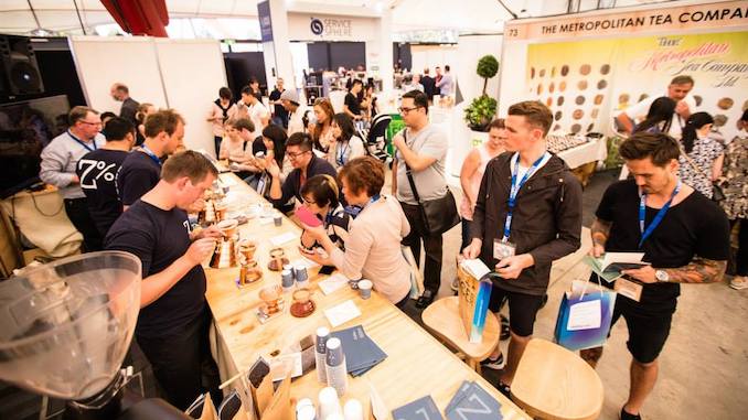 A group of people stand together tasting coffees at a conference.