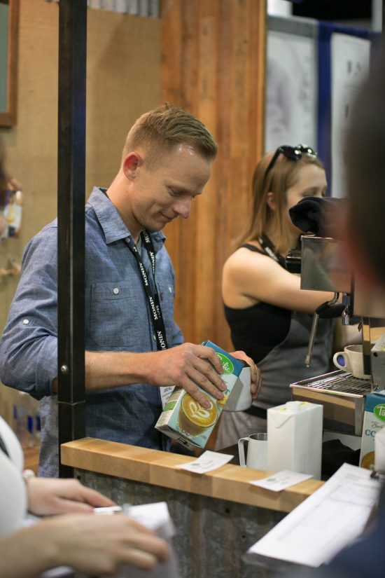A man with a long sleeve blue collared shirt pours almond milk into a pitcher at a booth.