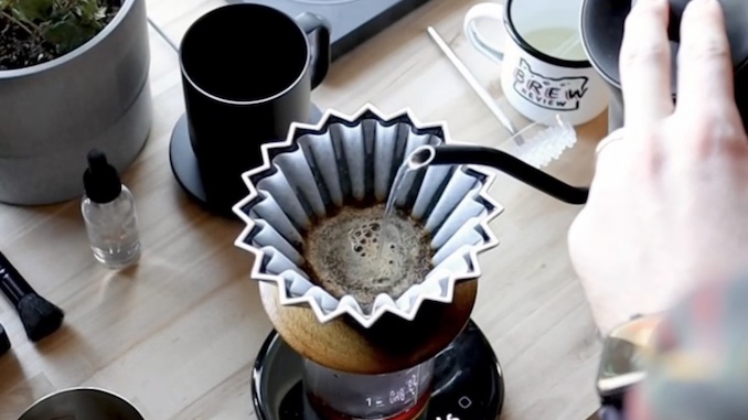 A closeup of a hand pouring water over a pourigami coffee cone.