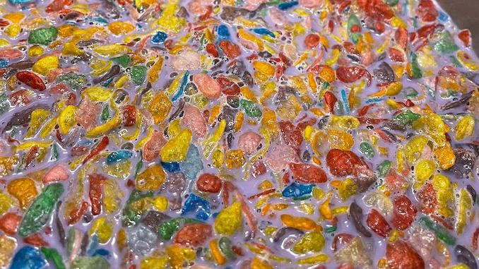 A closeup of colorful fruity pebbles cereal in purple milk in a silver mixing bowl.