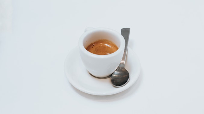 A simple white cup of espresso on a white background.